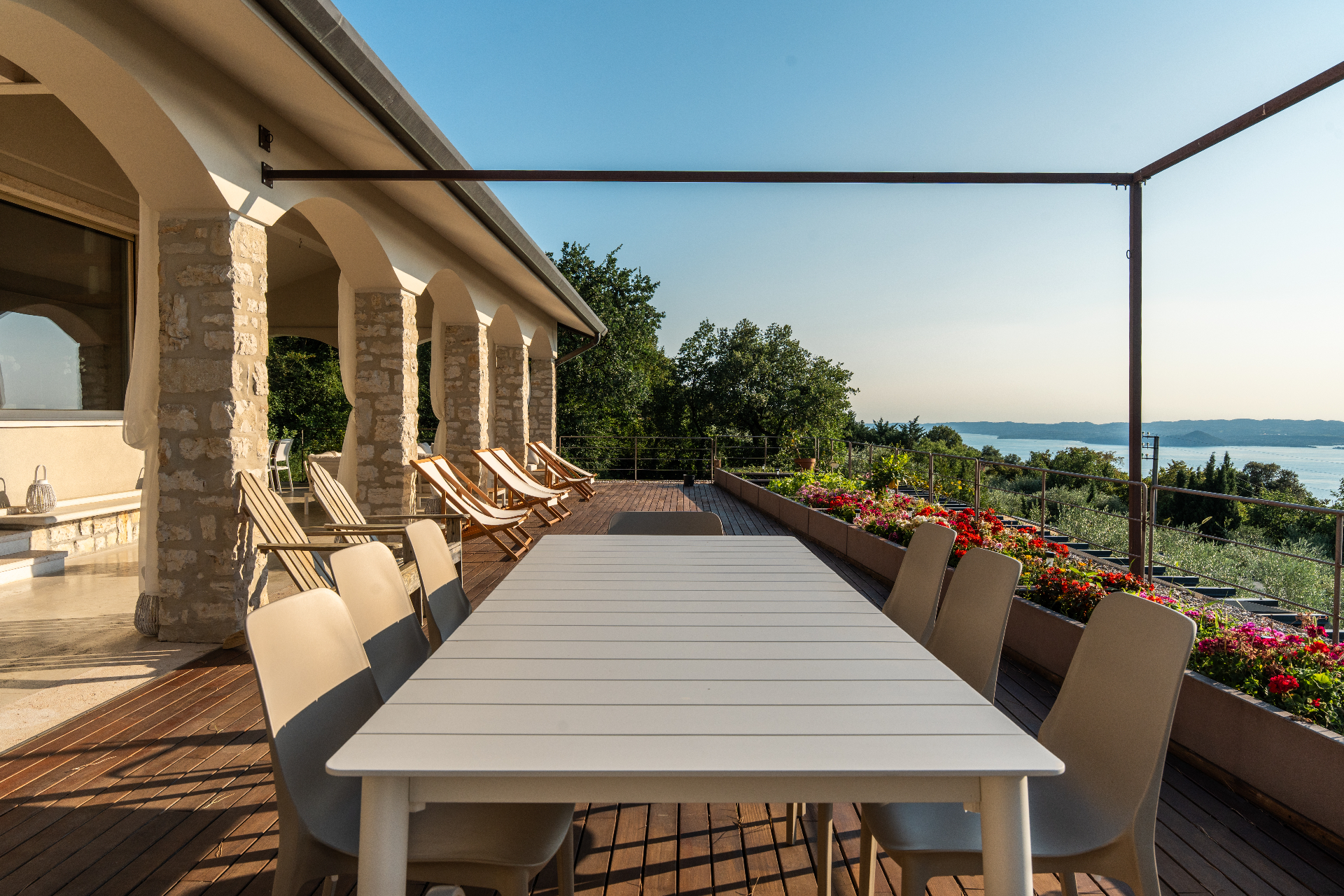 Covered terrace with long dining table and deckchairs overlooking Lake Garda