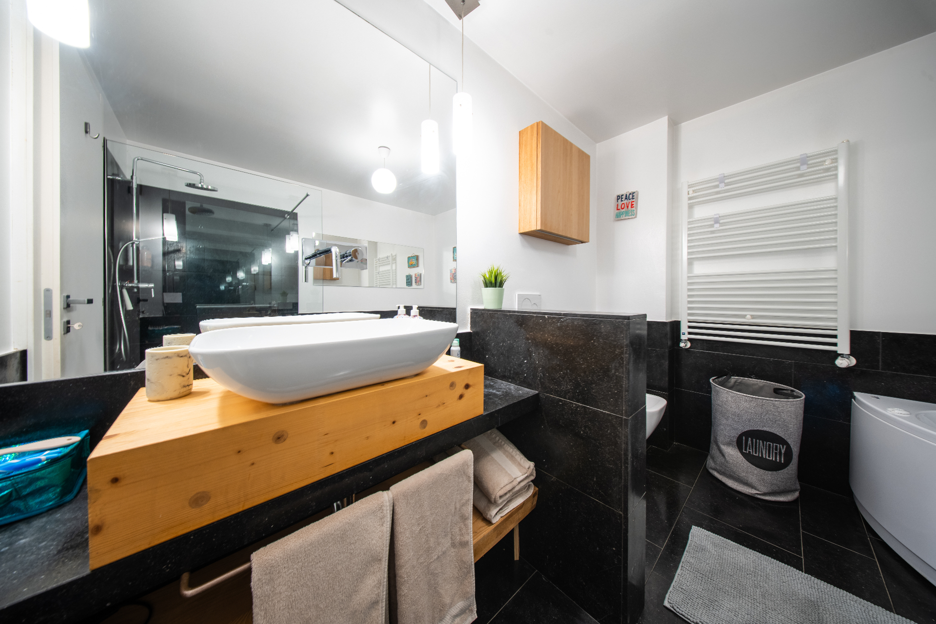 Black-tiled bathroom with wooden vanity and vessel basin