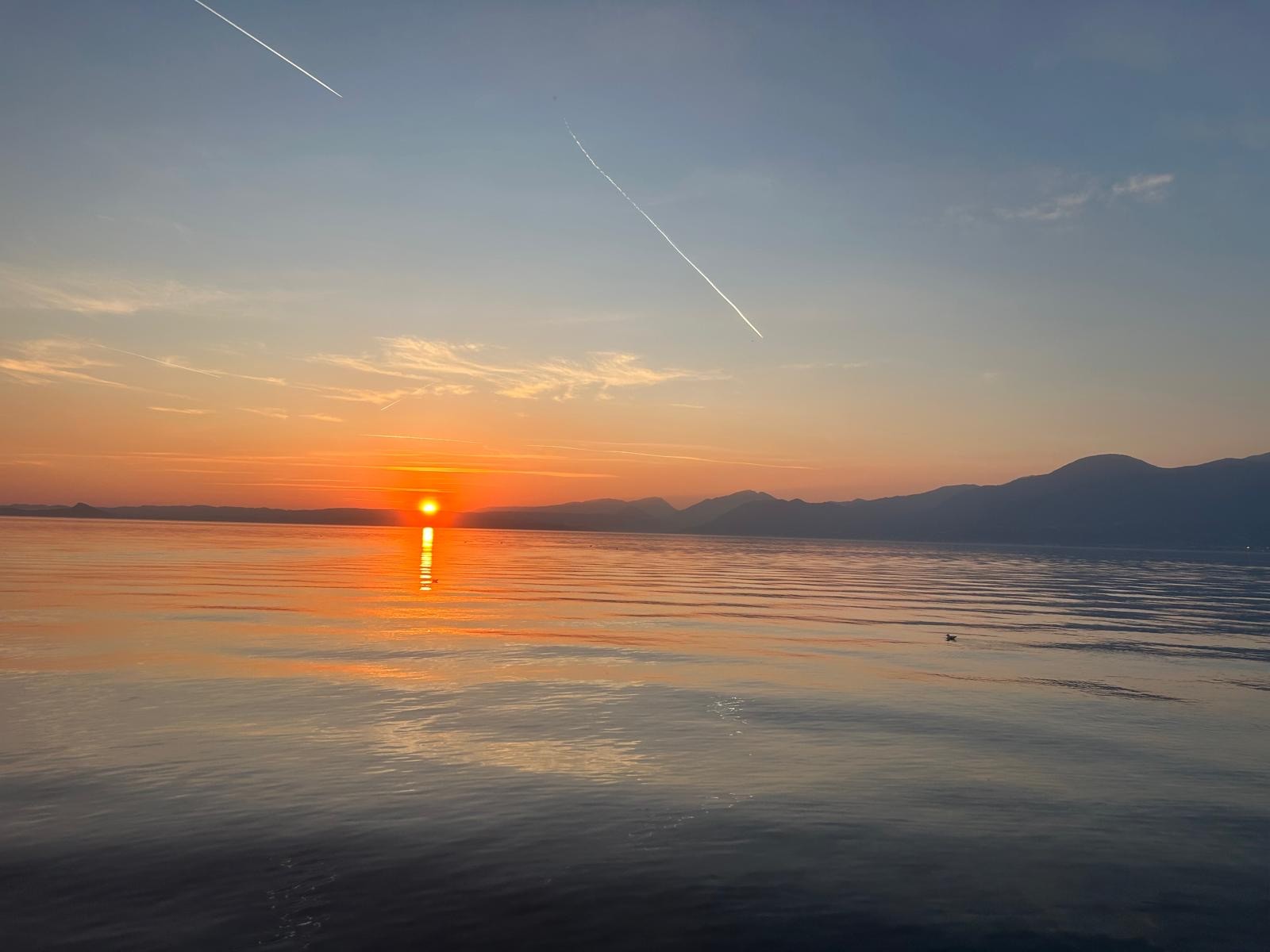 Golden Lake Garda sunset with jet contrails overhead